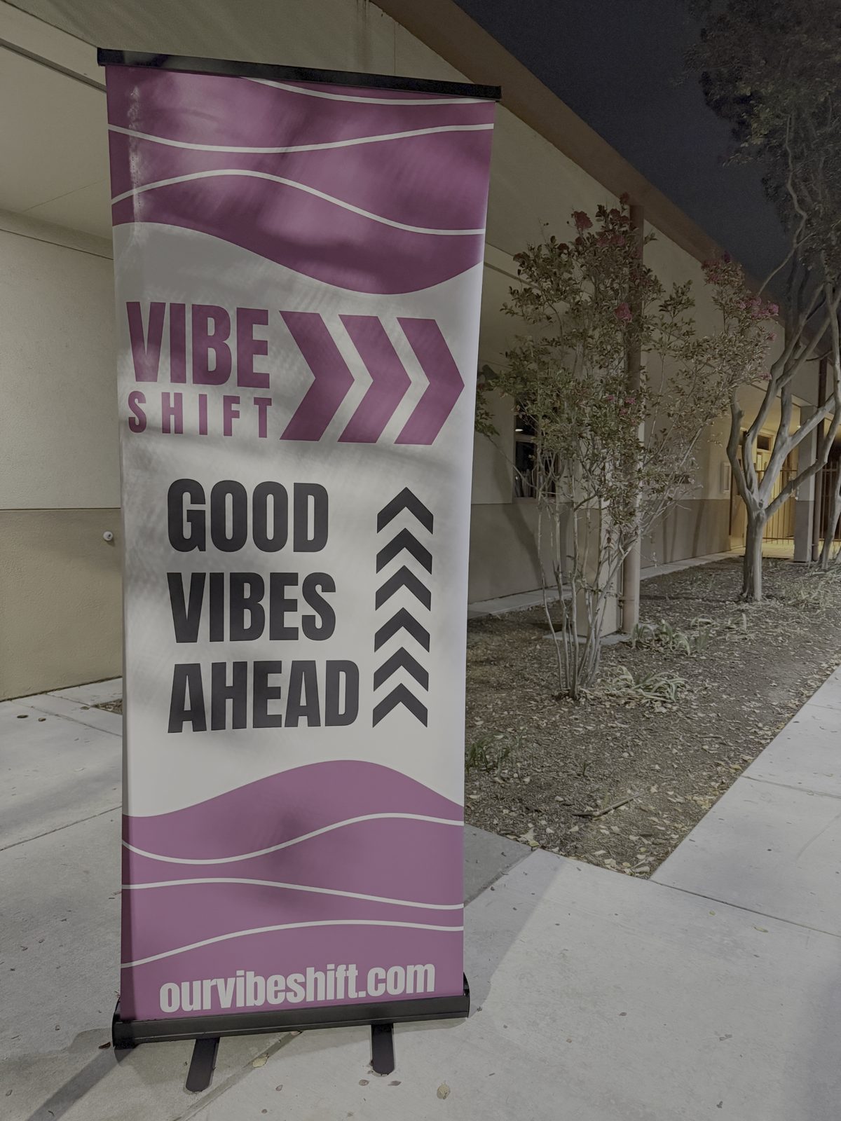 A "Good Vibes Ahead" Vibe Shift 2025 retractable banner with the ourvibeshift.com URL set up outside the Sacramento conference venue at dusk